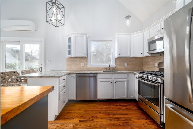 kitchen featuring pendant lighting, sink, appliances with stainless steel finishes, white cabinetry, and a wall mounted air conditioner