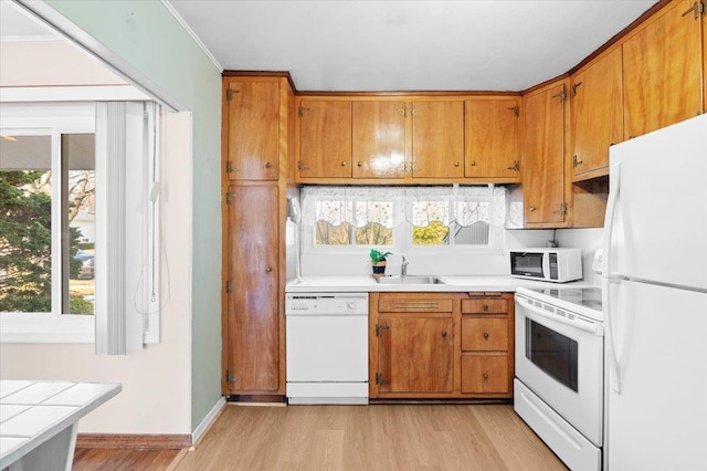 kitchen with sink, tile counters, light hardwood / wood-style floors, crown molding, and white appliances