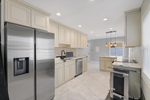 kitchen with appliances with stainless steel finishes, sink, decorative backsplash, hanging light fixtures, and cream cabinetry