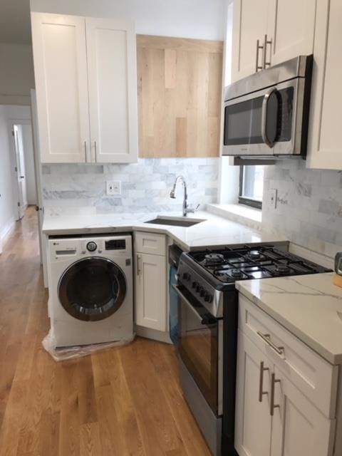 kitchen with sink, light hardwood / wood-style flooring, appliances with stainless steel finishes, white cabinets, and washer / clothes dryer