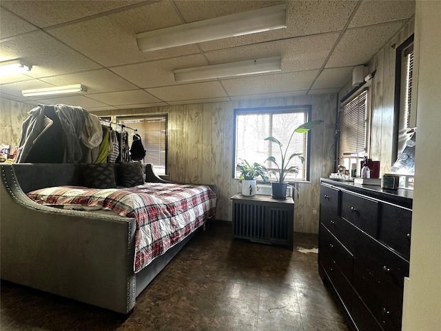 bedroom with radiator heating unit, a drop ceiling, and wood walls