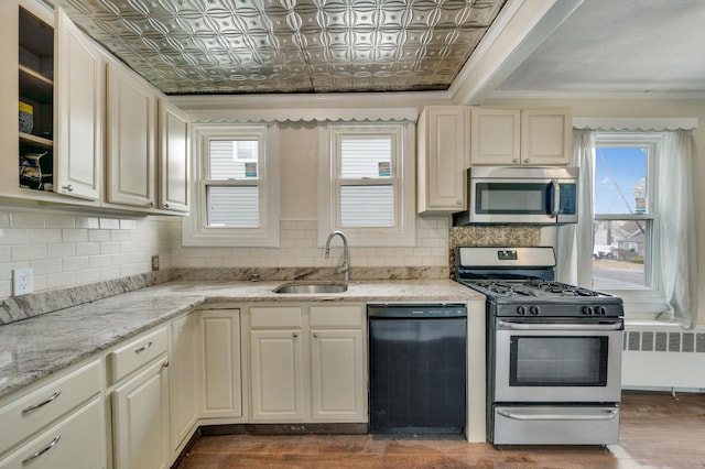 kitchen with radiator, sink, stainless steel appliances, tasteful backsplash, and light stone countertops