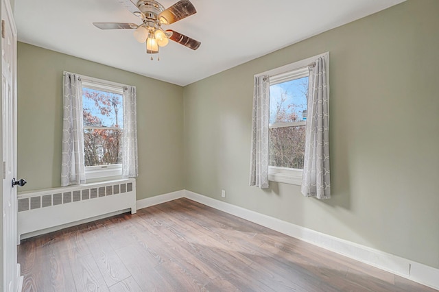 empty room with a healthy amount of sunlight, radiator, ceiling fan, and light hardwood / wood-style flooring