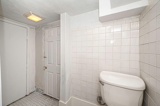 bathroom featuring toilet, a textured ceiling, and tile walls