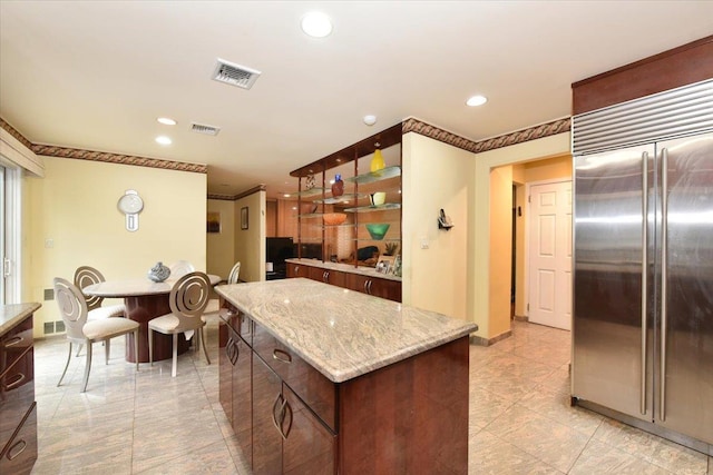 kitchen featuring built in refrigerator, recessed lighting, a kitchen island, light stone counters, and dark brown cabinetry