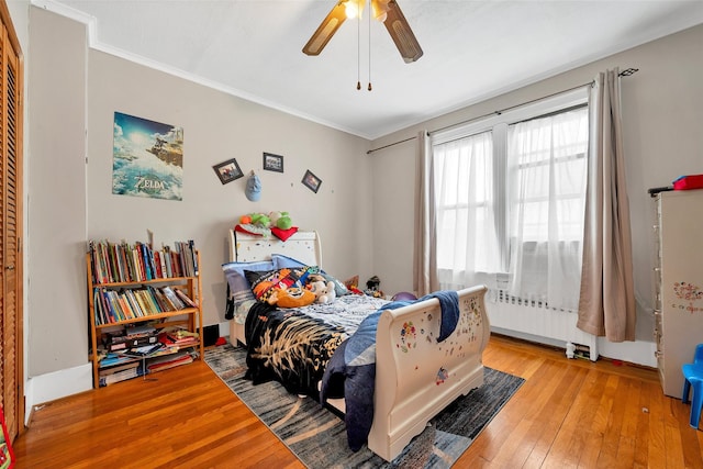 bedroom featuring hardwood / wood-style flooring, crown molding, radiator heating unit, and ceiling fan