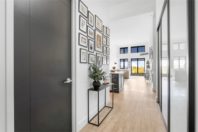 hall with light wood finished floors, a towering ceiling, and baseboards