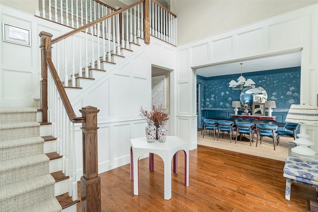 stairway featuring hardwood / wood-style flooring, ornamental molding, a chandelier, and a high ceiling