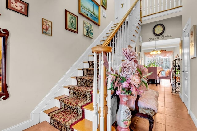 staircase featuring a towering ceiling, tile patterned floors, and a notable chandelier