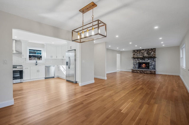 kitchen featuring appliances with stainless steel finishes, pendant lighting, tasteful backsplash, white cabinets, and wall chimney range hood