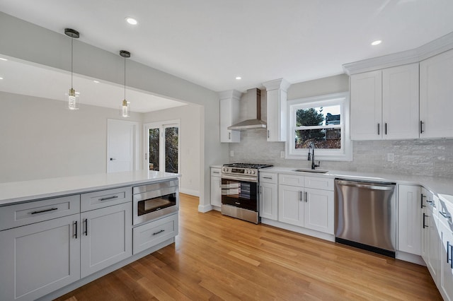 kitchen with appliances with stainless steel finishes, decorative light fixtures, white cabinets, light hardwood / wood-style floors, and wall chimney exhaust hood