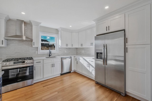 kitchen with appliances with stainless steel finishes, white cabinetry, sink, light hardwood / wood-style floors, and wall chimney exhaust hood