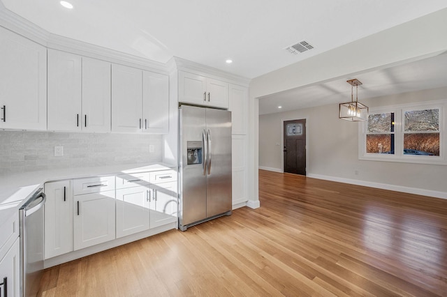 kitchen featuring pendant lighting, appliances with stainless steel finishes, light wood-type flooring, and white cabinets