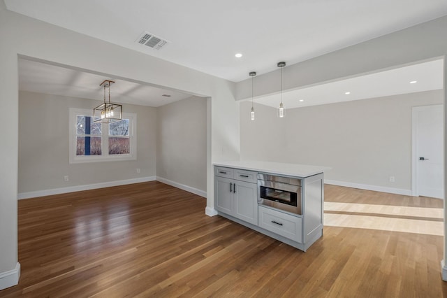 kitchen with a notable chandelier, pendant lighting, stainless steel microwave, and light hardwood / wood-style flooring