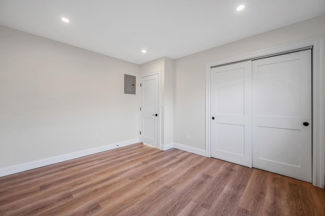 unfurnished bedroom featuring electric panel, light hardwood / wood-style floors, and a closet