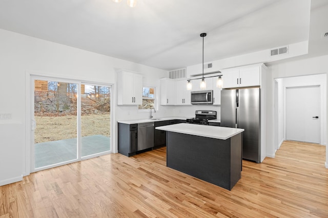 kitchen with a kitchen island, appliances with stainless steel finishes, white cabinets, hanging light fixtures, and light hardwood / wood-style floors