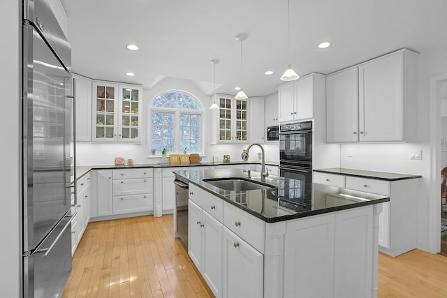 kitchen with light wood finished floors, an island with sink, stainless steel appliances, white cabinetry, and a sink