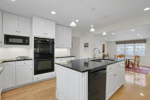 kitchen featuring a sink, white cabinetry, light wood-type flooring, black appliances, and a center island with sink