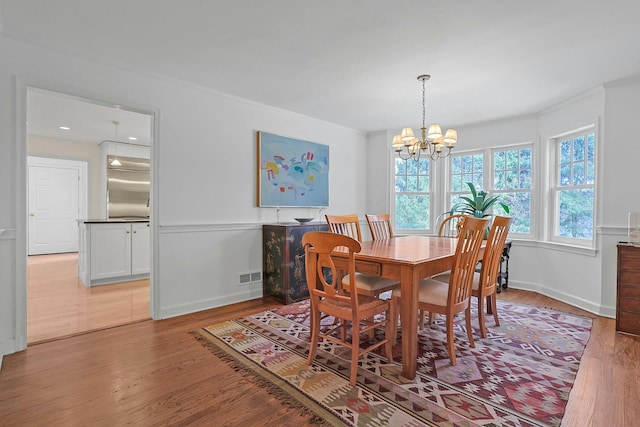 dining room with light wood-type flooring, a notable chandelier, visible vents, and crown molding