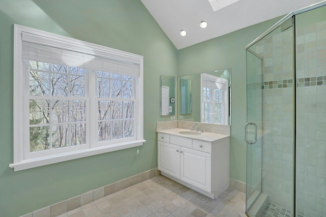 bathroom featuring vaulted ceiling with skylight, baseboards, a shower stall, and vanity