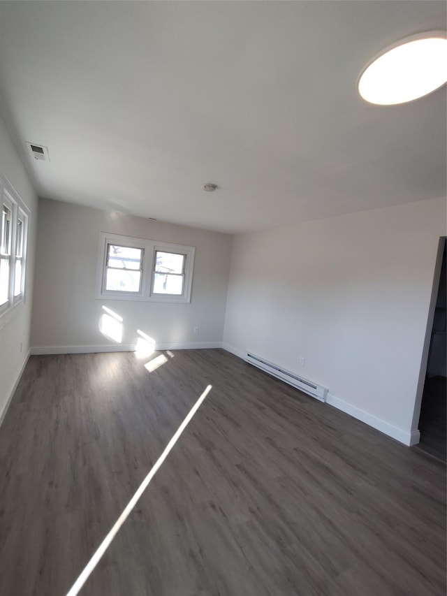 empty room featuring baseboard heating and dark wood-type flooring