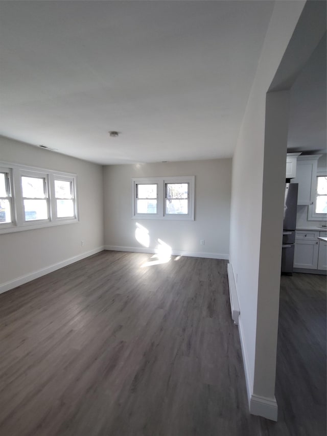 empty room with a baseboard heating unit, plenty of natural light, and dark hardwood / wood-style floors