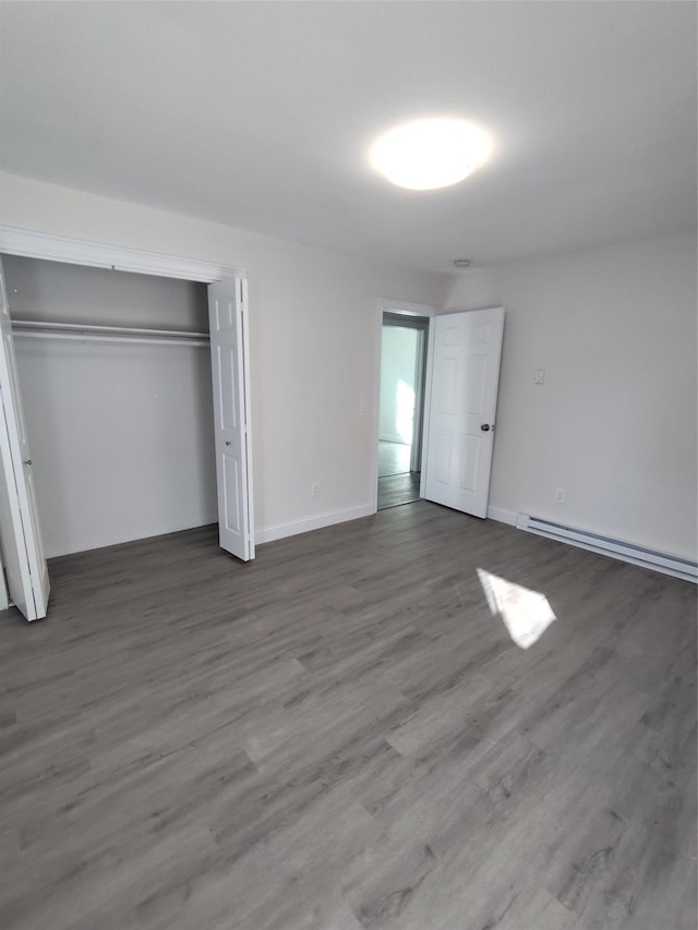 unfurnished bedroom featuring a baseboard radiator, dark hardwood / wood-style floors, and a closet