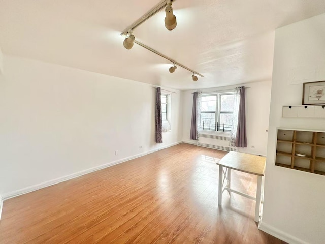 unfurnished living room featuring hardwood / wood-style floors, radiator heating unit, and rail lighting