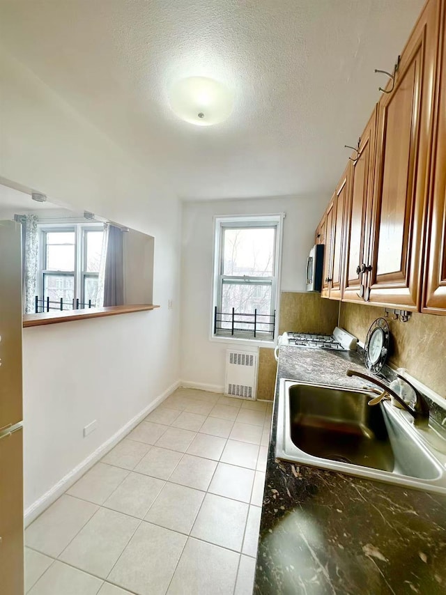 kitchen with light tile patterned flooring, sink, a textured ceiling, radiator, and dark stone counters