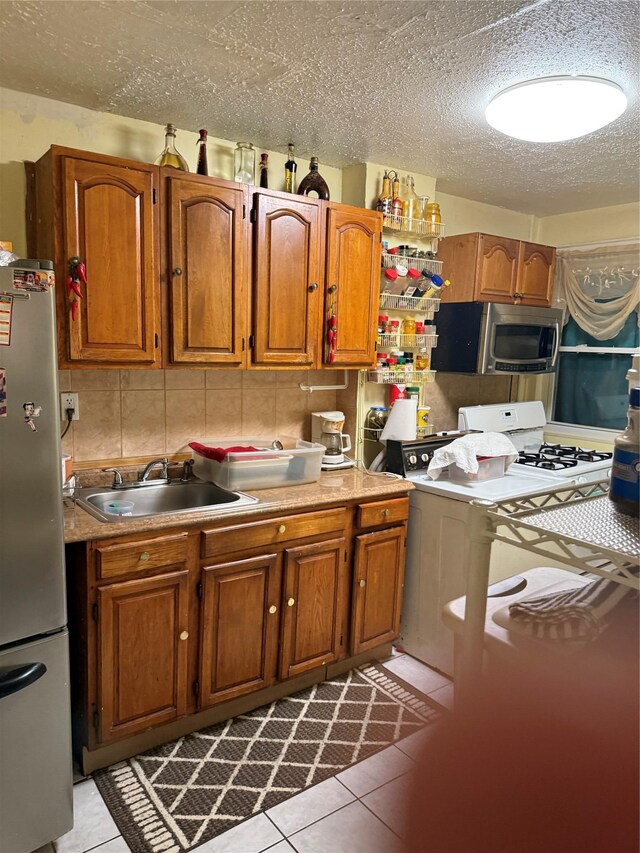 kitchen featuring tile patterned flooring, a sink, brown cabinets, and stainless steel appliances
