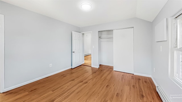 unfurnished bedroom featuring a baseboard heating unit, light hardwood / wood-style flooring, a closet, and vaulted ceiling