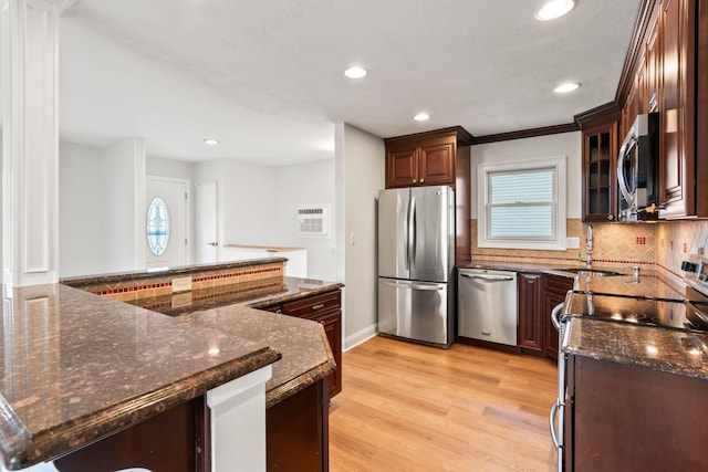 kitchen with tasteful backsplash, light hardwood / wood-style flooring, appliances with stainless steel finishes, kitchen peninsula, and dark stone counters