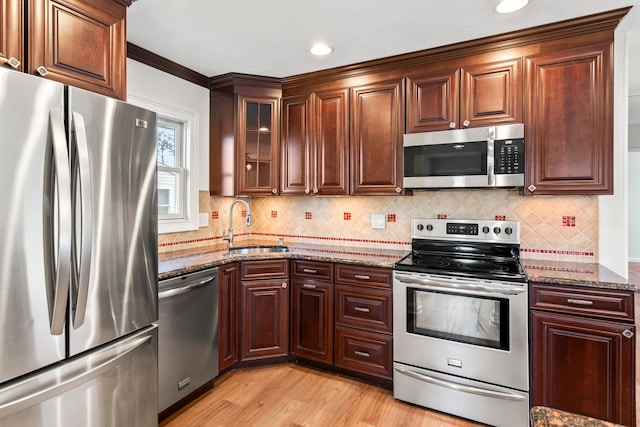 kitchen featuring sink, appliances with stainless steel finishes, decorative backsplash, dark stone counters, and light wood-type flooring