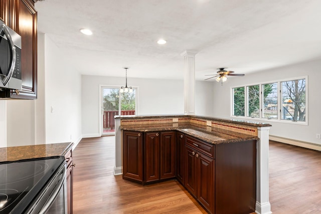 kitchen featuring ceiling fan with notable chandelier, light hardwood / wood-style floors, kitchen peninsula, decorative light fixtures, and dark stone counters