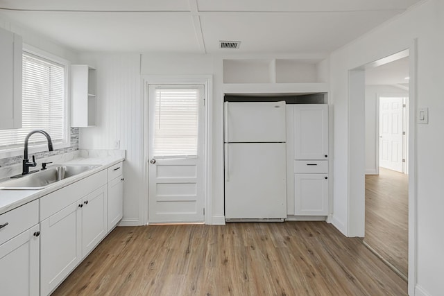 kitchen with white cabinetry, white fridge, sink, and light hardwood / wood-style flooring