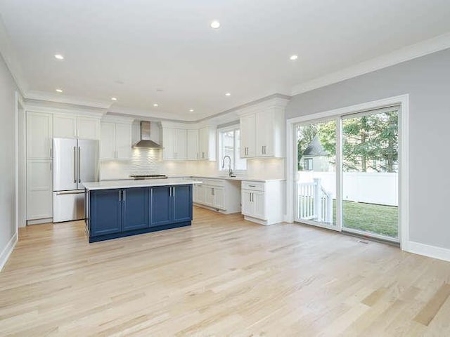 kitchen with high end fridge, tasteful backsplash, white cabinets, a kitchen island, and wall chimney exhaust hood