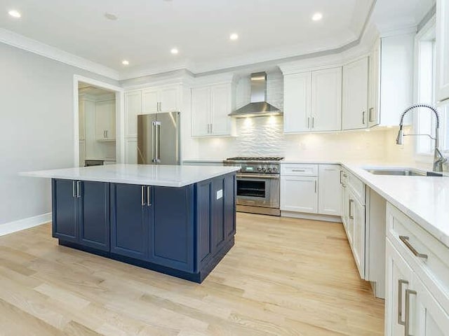 kitchen featuring wall chimney exhaust hood, sink, high end appliances, white cabinetry, and a center island