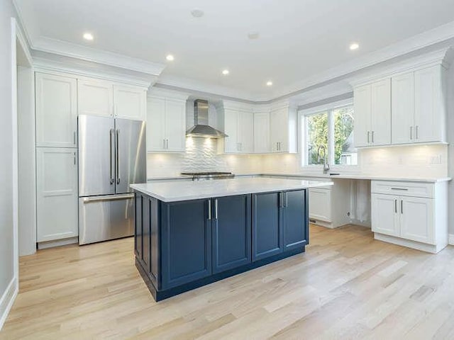 kitchen with high quality fridge, white cabinets, a center island, light hardwood / wood-style floors, and wall chimney range hood