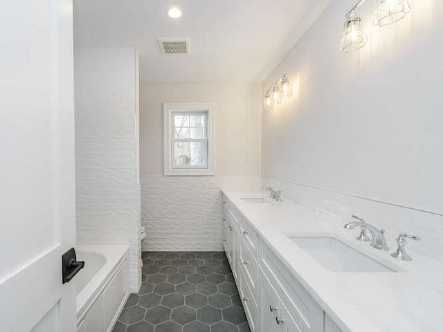 bathroom with a washtub, tile walls, vanity, tile patterned floors, and toilet