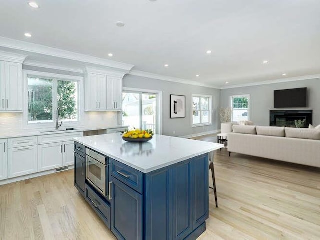 111 Fairfield Ave, Port Washington, NY 11050 - kitchen with light wood-style flooring, a sink, white cabinetry, stainless steel microwave, and backsplash