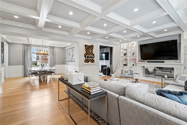 living room with built in features, a premium fireplace, an inviting chandelier, light wood-style floors, and beam ceiling