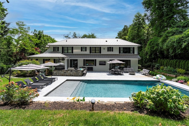 back of house featuring an outdoor pool, a standing seam roof, a patio area, and metal roof