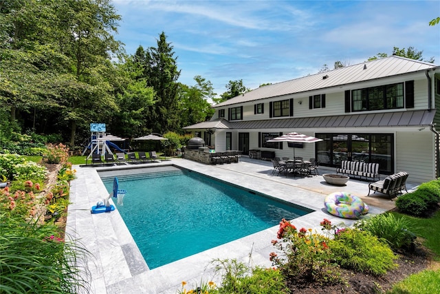 outdoor pool with an outdoor living space with a fire pit, a playground, and a patio