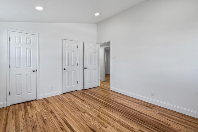 unfurnished bedroom with lofted ceiling, two closets, and light wood-type flooring