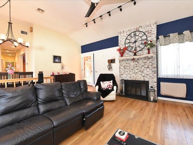 living room featuring vaulted ceiling, a brick fireplace, hardwood / wood-style floors, and track lighting