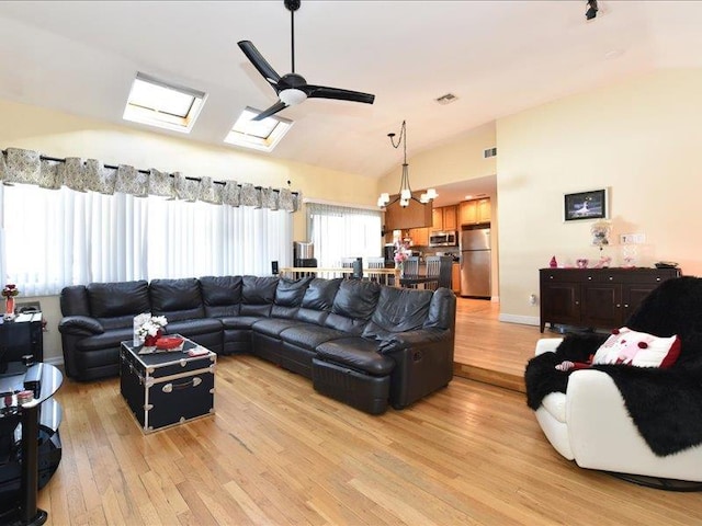 living room with ceiling fan, light hardwood / wood-style floors, and vaulted ceiling with skylight