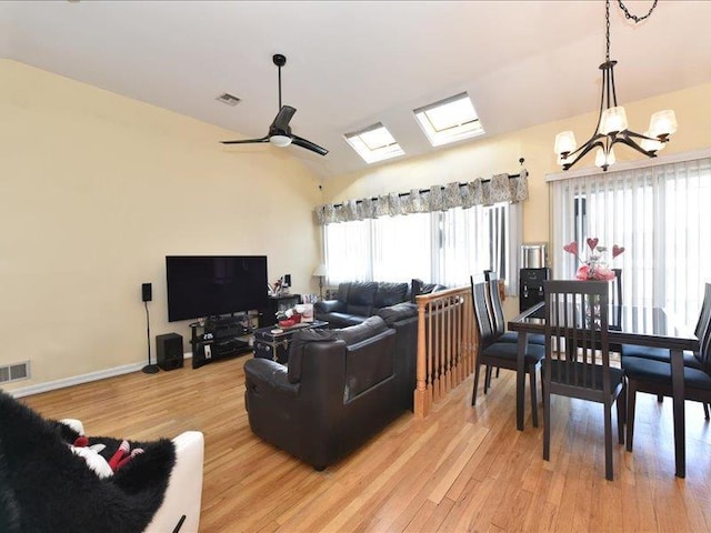 living room featuring vaulted ceiling with skylight, ceiling fan with notable chandelier, and light hardwood / wood-style flooring