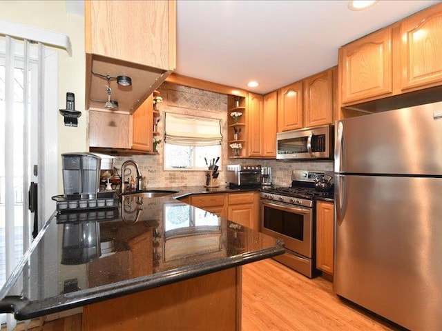 kitchen featuring sink, light hardwood / wood-style flooring, appliances with stainless steel finishes, dark stone countertops, and kitchen peninsula