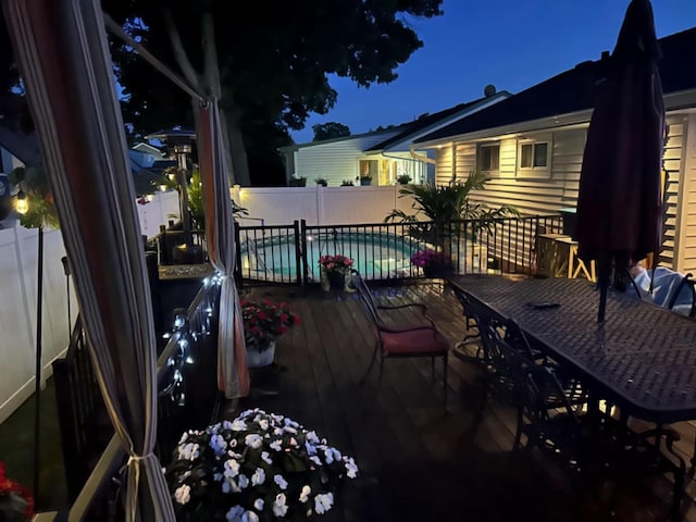 deck at night with a fenced in pool