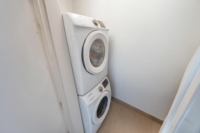 clothes washing area featuring baseboards, stacked washer and dryer, laundry area, and tile patterned floors